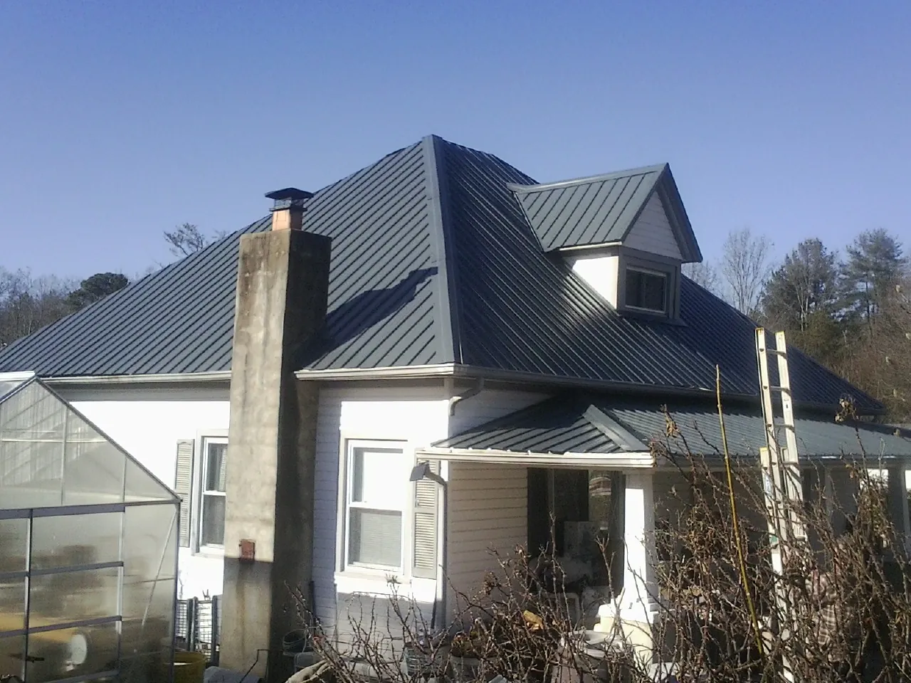 Dark blue standing seam metal roof on a white farmhouse with dormer — Slate & Tile Roof Repair by Roofing Brothers in Farrell