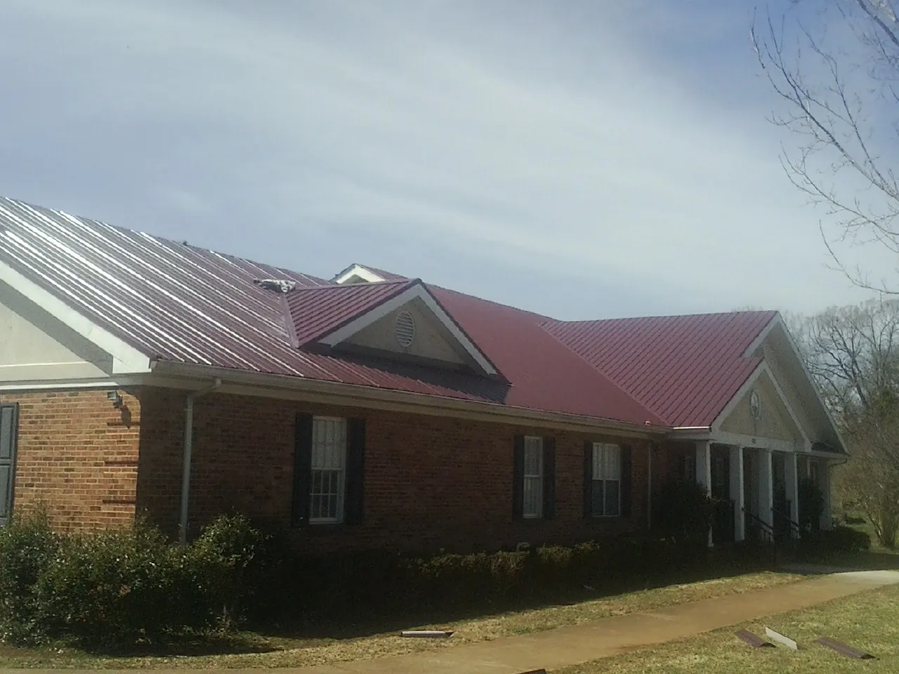 Red metal roof with gabled entries on a long brick building, from a Hail Damage Roof Repair job in Farrell