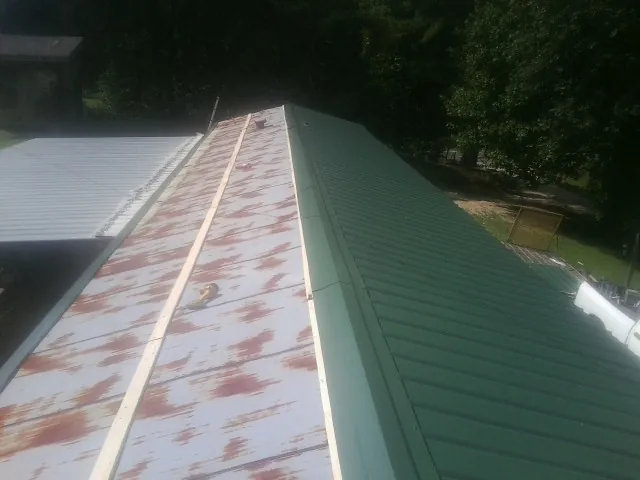 Old rusted panels beside newly installed green metal roofing — Wind Damage Roof Repair by Roofing Brothers in Farrell