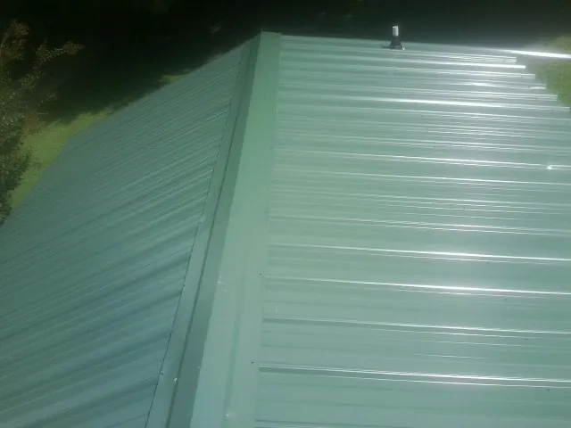 New green metal panels meeting at the ridge of a roof — Flat Roof Repair work by our crew in Farrell
