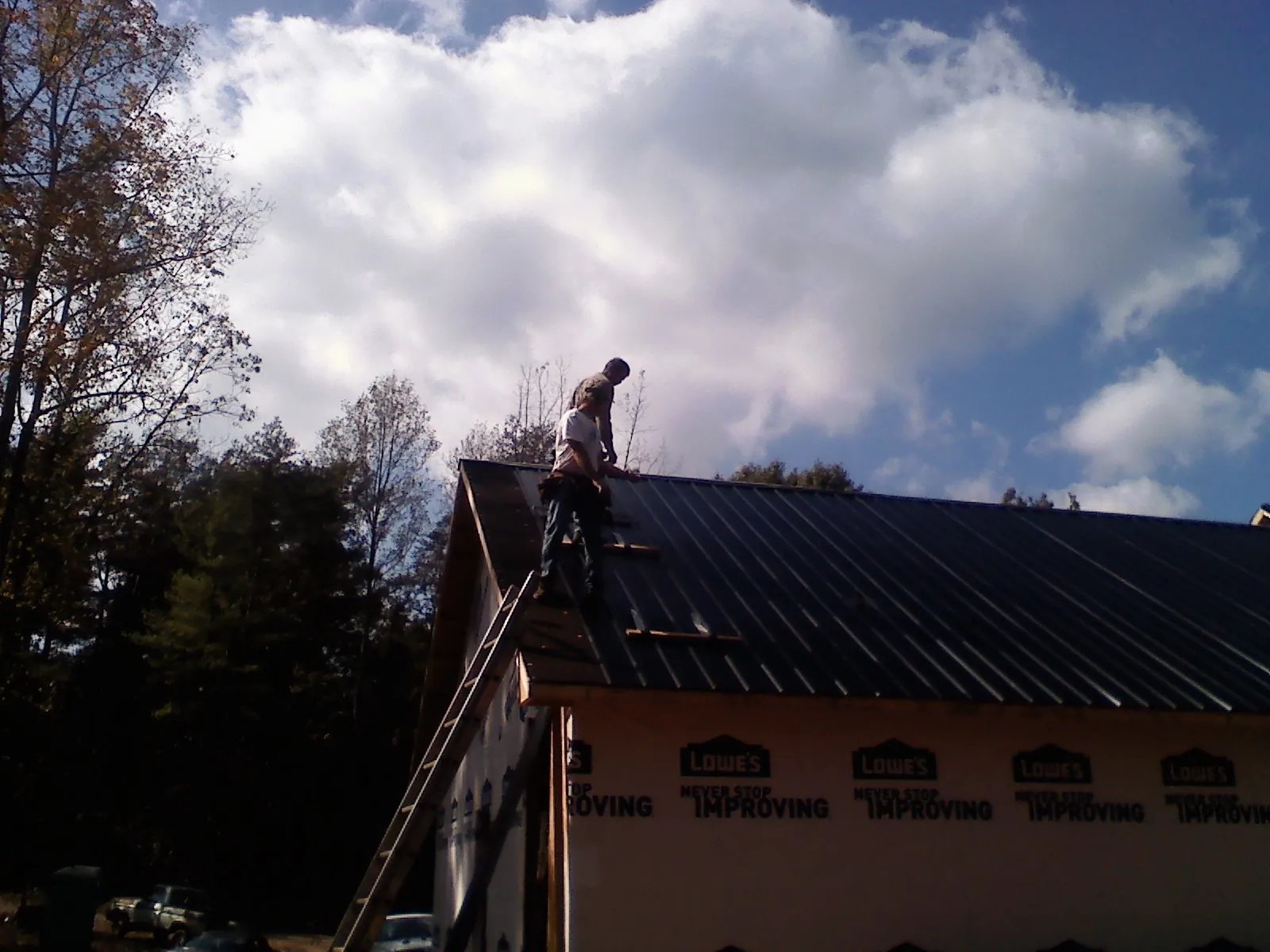 Roofer fastening dark metal panels high against a cloudy sky, from a Roof Inspection job in Farrell