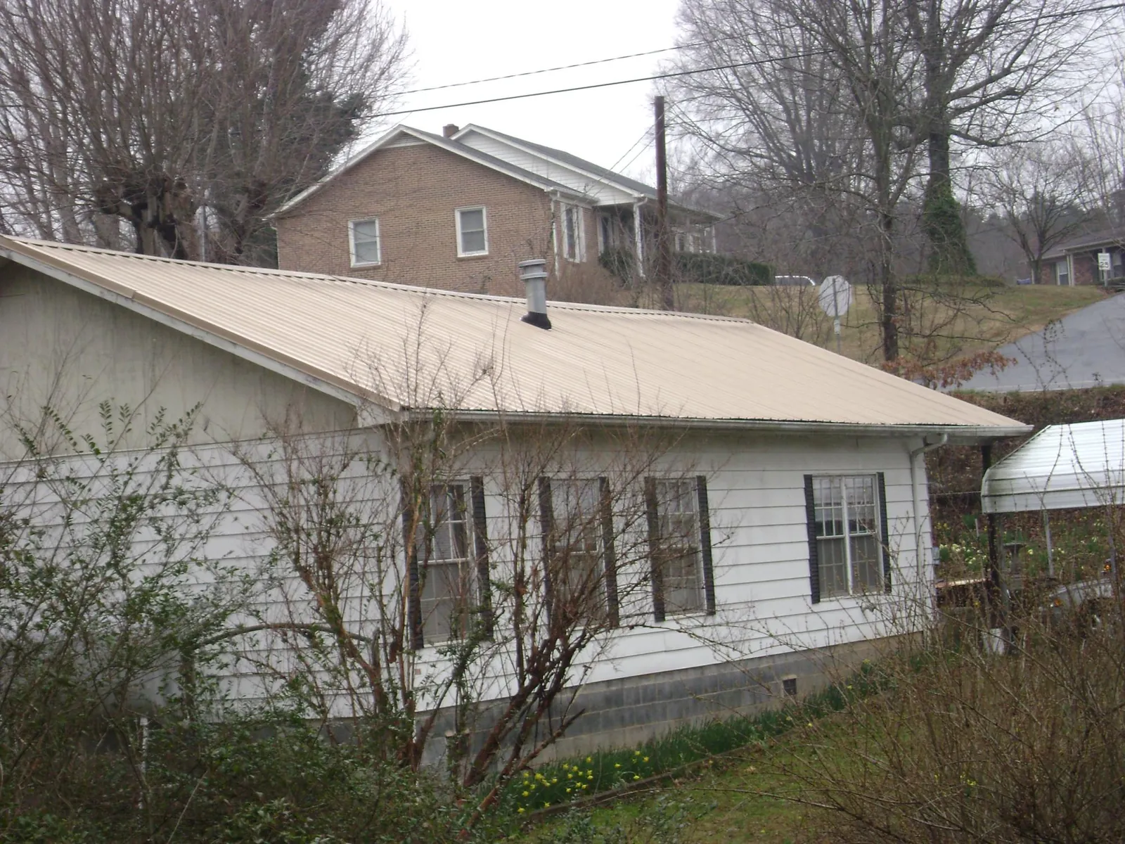 Tan metal roof on a white sided house set into a hillside — Commercial Roofing by Roofing Brothers in Farrell